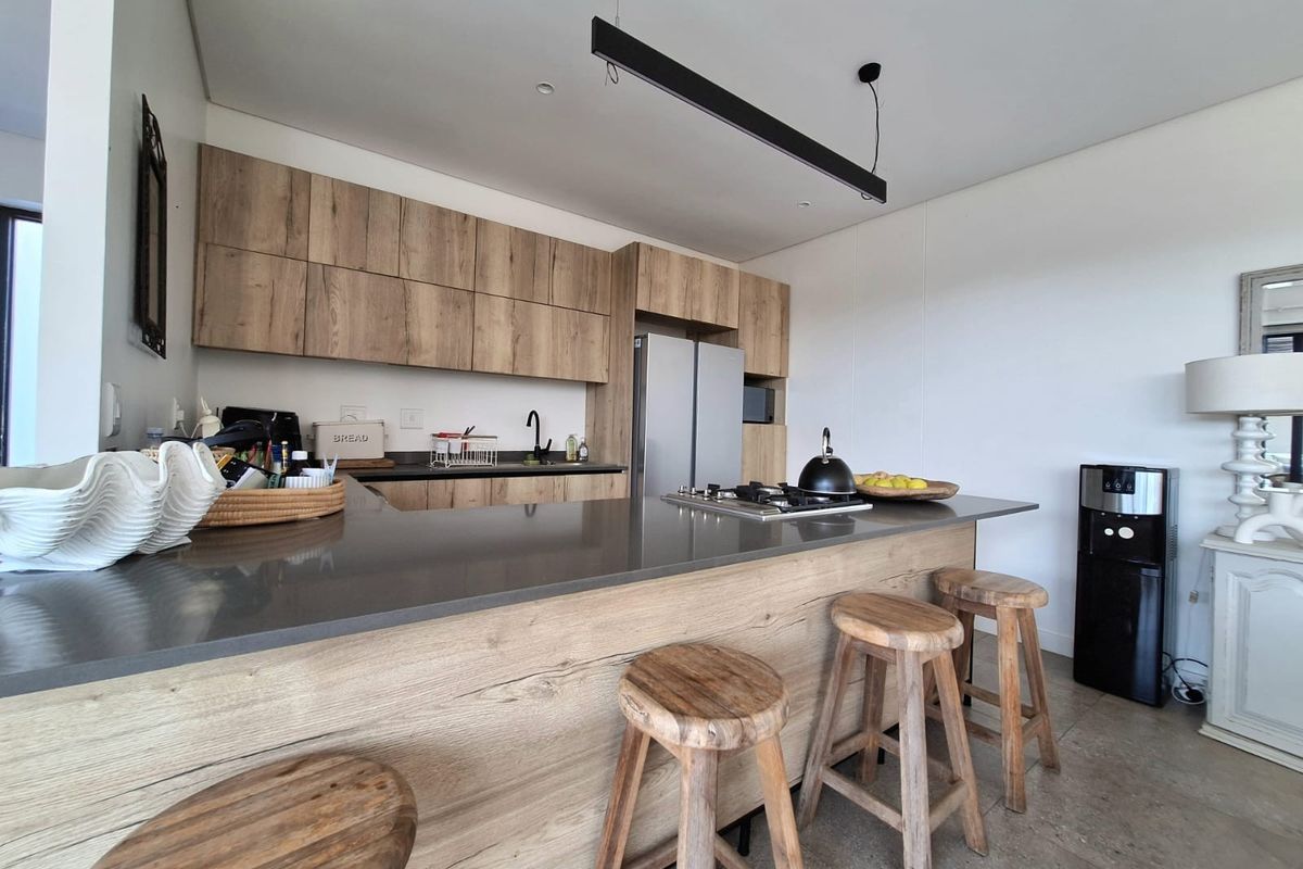 Modern kitchen featuring wood-grain cabinetry, stone countertops, a breakfast bar, and a built-in gas hob with integrated appliances.