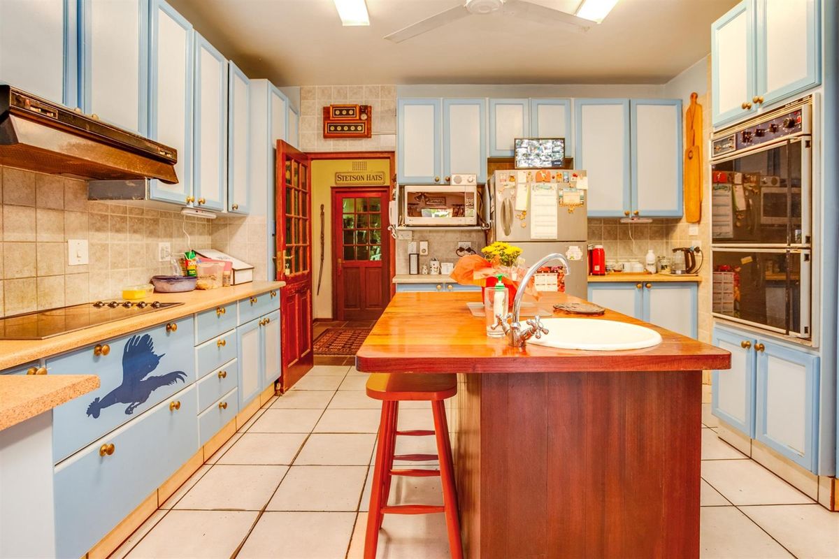 A spacious kitchen featuring light blue cabinetry, a central wooden island with a prep sink, built-in double ovens, and tiled flooring.