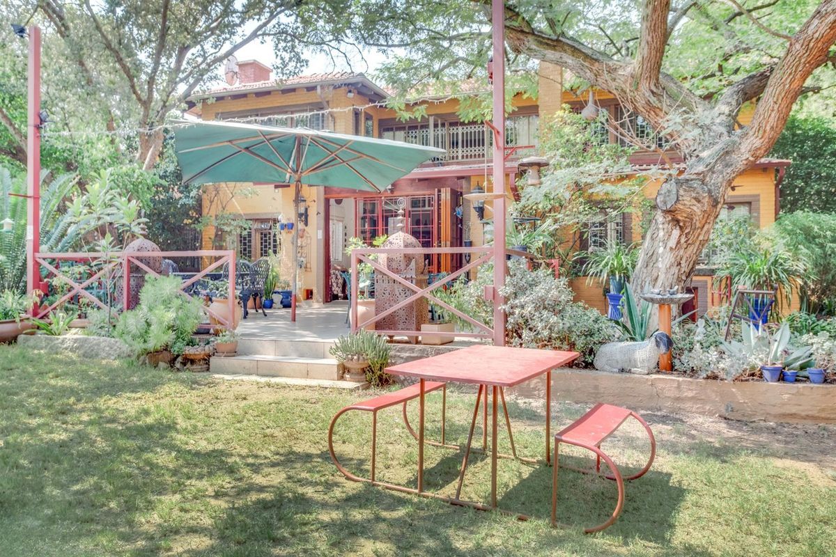 A view of the rear exterior of the guest house, featuring a paved patio area, established garden, and mature trees.