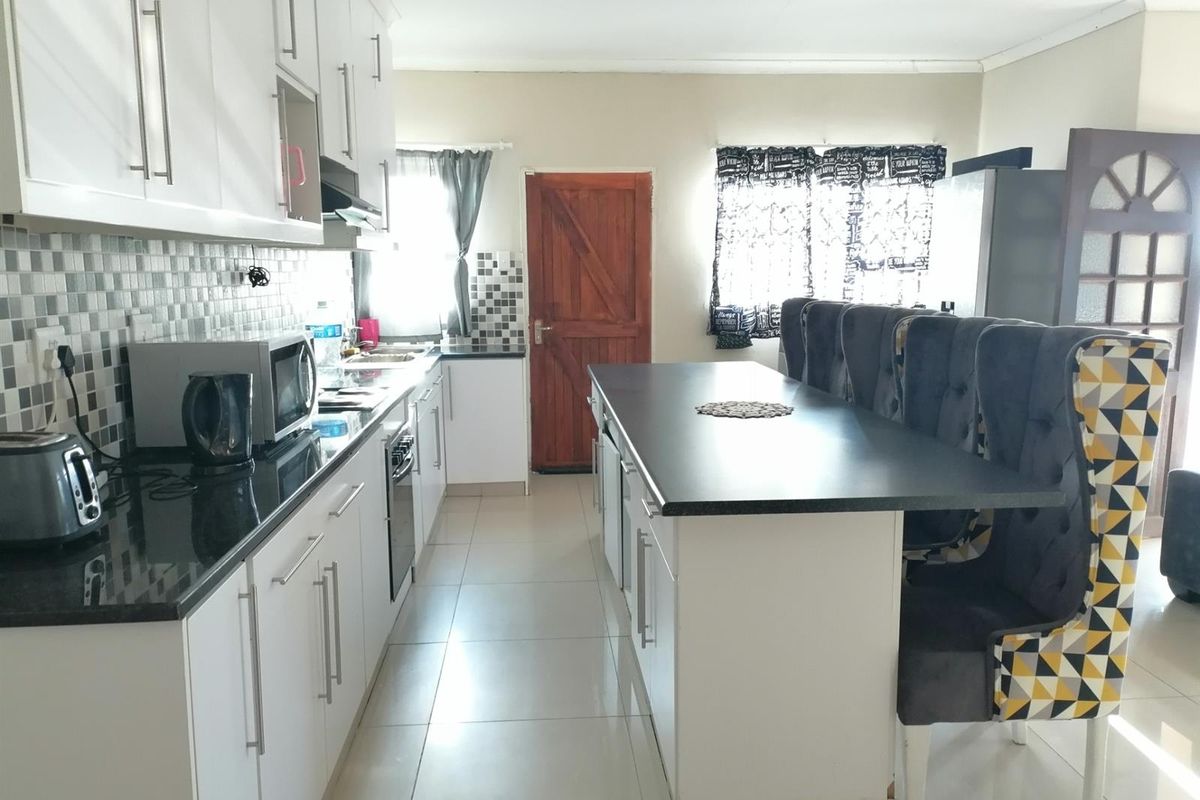 A functional kitchen featuring white cabinetry, dark countertops, a central island, and tiled flooring, providing a practical workspace for daily meal preparation.
