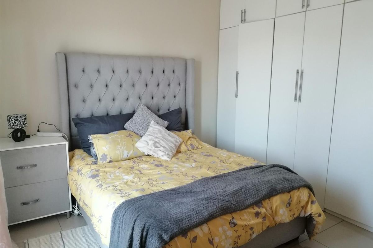 A well-maintained bedroom featuring built-in floor-to-ceiling wardrobes with modern white cabinetry and tiled flooring.