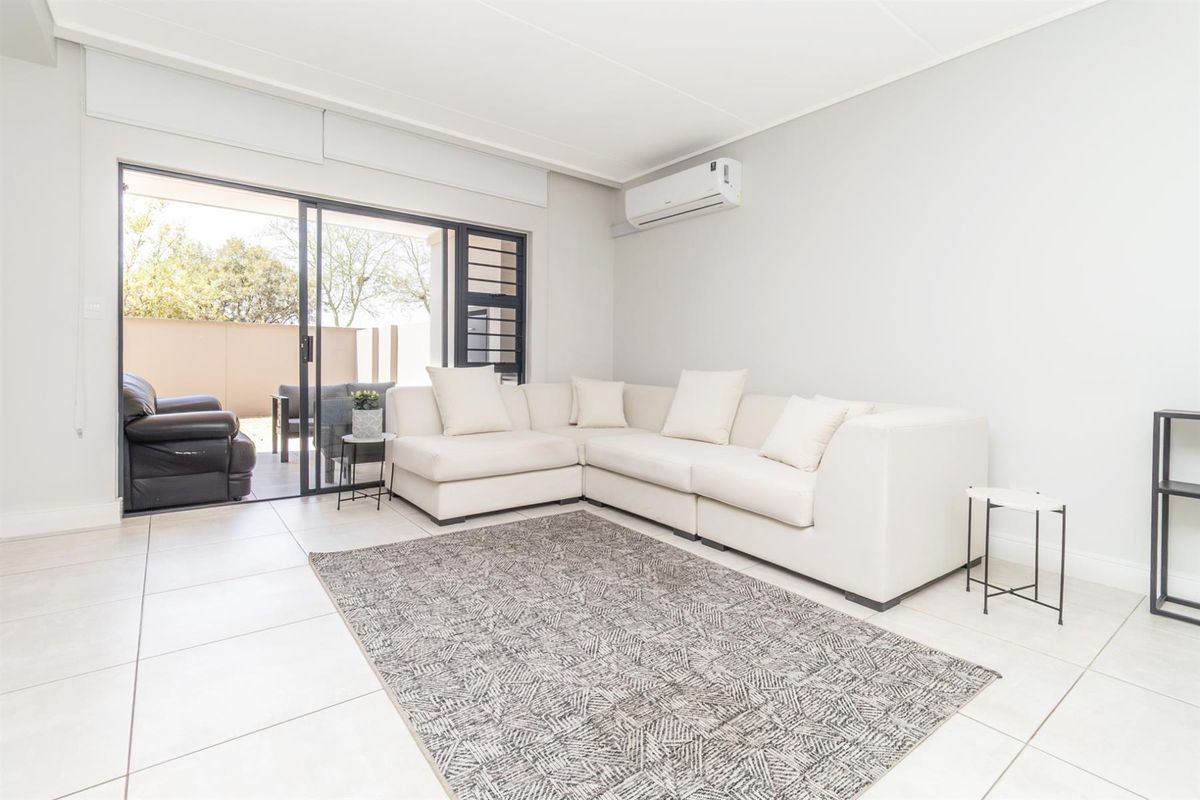 Bright living room featuring tiled flooring, a wall-mounted air conditioning unit, and large sliding glass doors providing access to an outdoor patio area.
