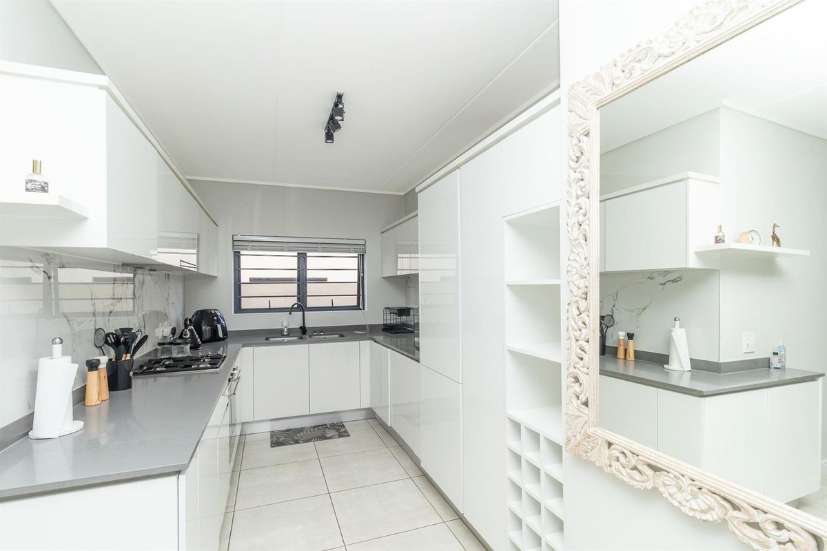 Modern kitchen featuring sleek white cabinetry, stone countertops, a gas hob, and a double sink with a contemporary black faucet.