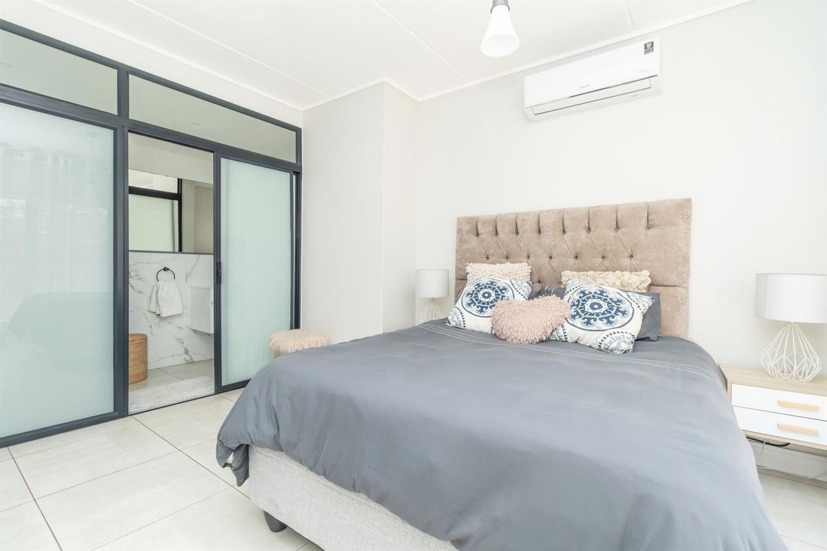 A modern bedroom featuring tiled flooring, a wall-mounted air conditioning unit, and an en-suite bathroom accessed through a contemporary sliding glass door partition.