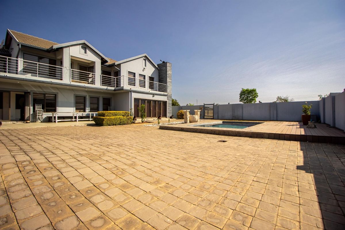 Spacious rear exterior featuring a large paved patio, a built-in swimming pool, and a double-story house with balcony access.