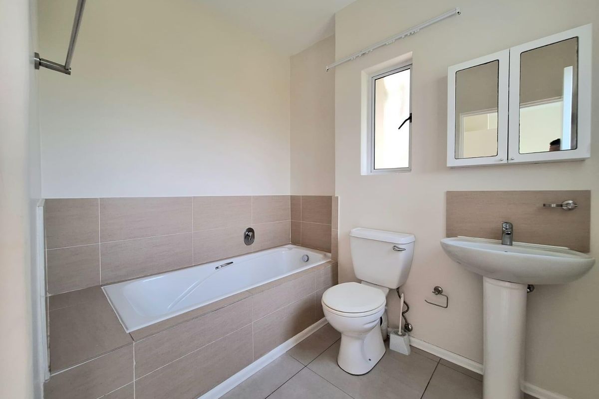 A clean, functional bathroom featuring a tiled bathtub surround, pedestal sink, wall-mounted medicine cabinet, and a standard toilet.