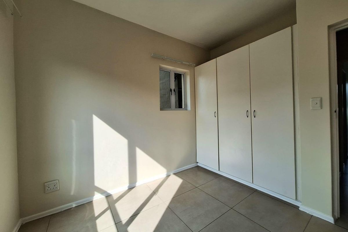 A bright, empty bedroom featuring neutral tiled flooring, built-in white cabinetry, and a small window allowing natural light.