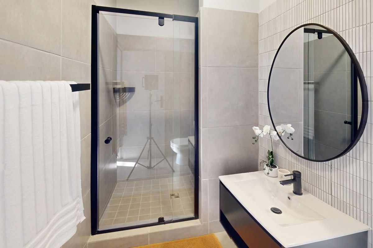 Modern bathroom featuring a walk-in shower with black-framed glass, a sleek wall-mounted vanity with integrated basin, and contemporary tiled finishes.