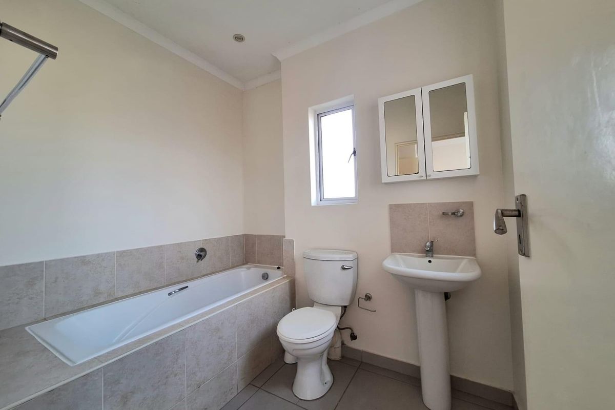 A functional bathroom featuring a built-in bathtub with tiled surround, a pedestal sink, a toilet, and a wall-mounted mirrored medicine cabinet.