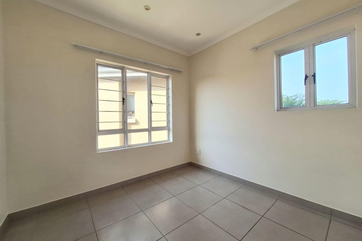 A bright, empty bedroom featuring neutral tiled flooring, recessed ceiling lighting, and security bars on the windows.
