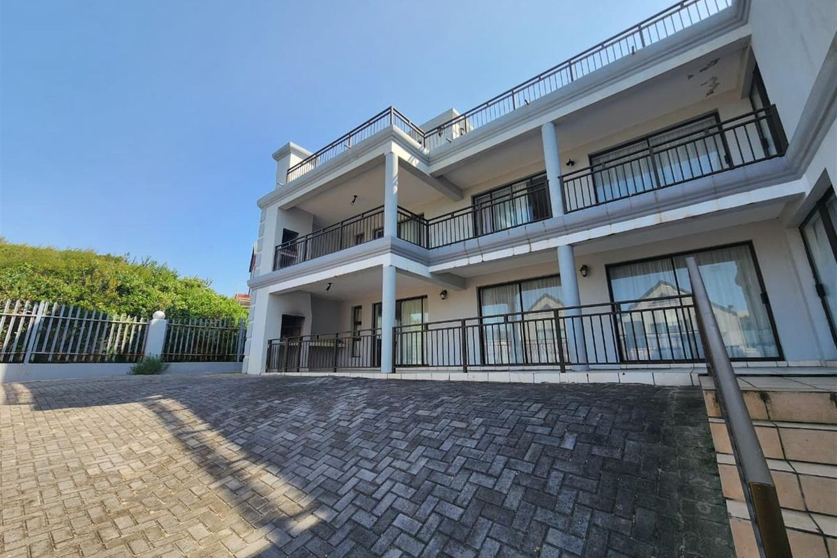 A multi-level rear exterior view of the property featuring paved driveway access, tiered balconies with metal railings, and large sliding glass doors.