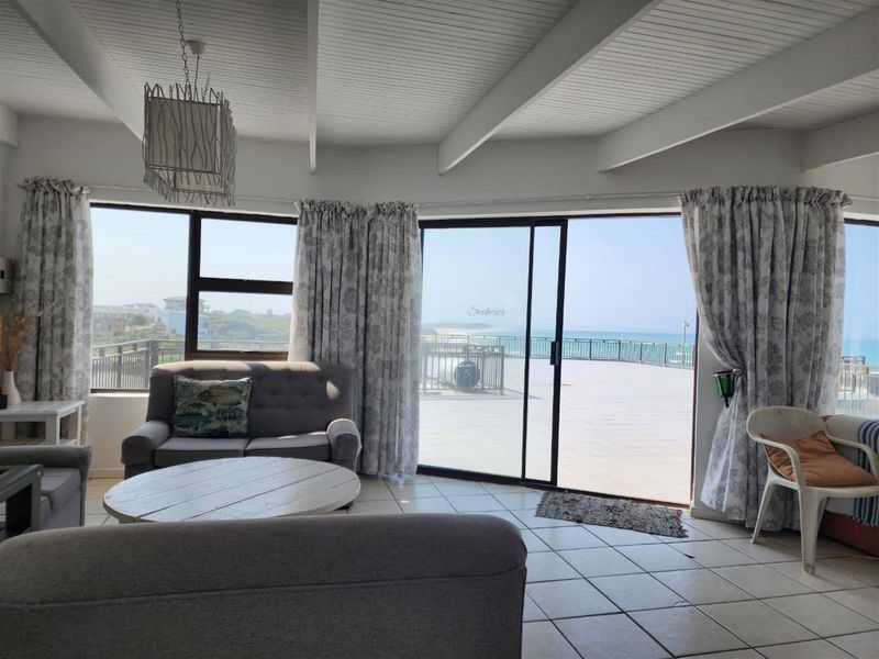 Spacious living area featuring tiled floors, exposed beam ceilings, and large sliding glass doors that open onto a balcony with ocean views.