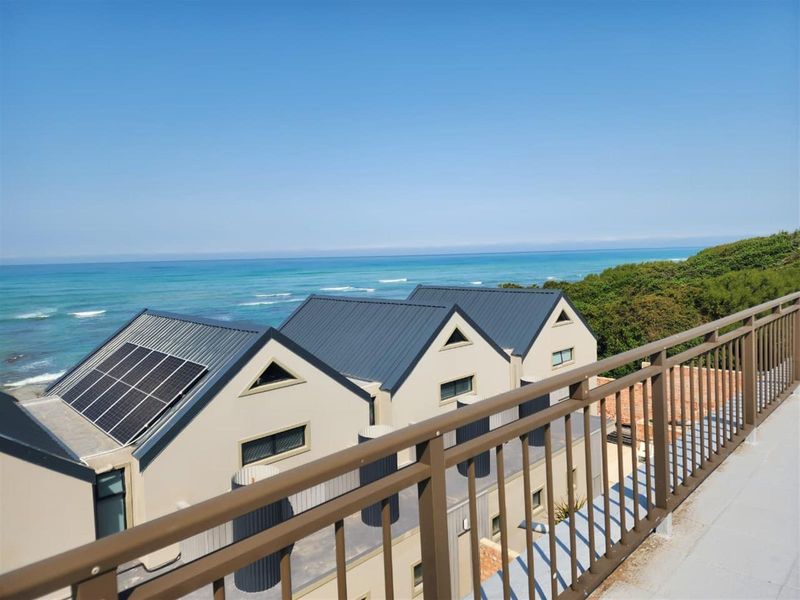 Elevated view overlooking the property's metal roof structure with solar panels, featuring a balcony railing and a scenic ocean backdrop.