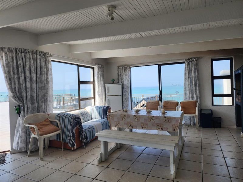 Spacious living area featuring tiled floors, exposed beam ceilings, and large sliding glass doors offering expansive ocean views.