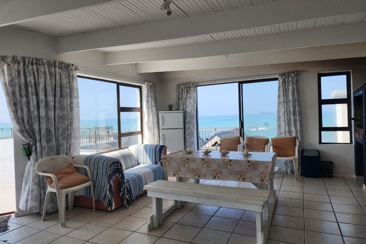 Spacious living area featuring tiled floors, exposed beam ceilings, and large sliding glass doors offering expansive ocean views.