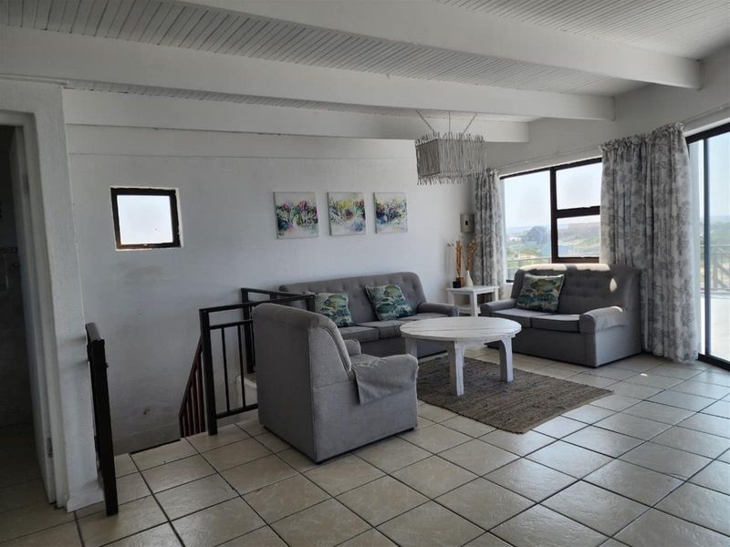 A bright living room featuring tiled flooring, exposed beam ceilings, and a staircase with metal railing, leading to large sliding doors with natural light.
