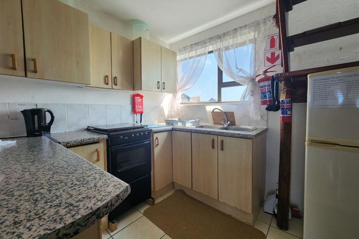 Compact kitchen featuring laminate cabinetry, granite-look countertops, tiled backsplash, and a functional layout with a stainless steel sink and freestanding oven.