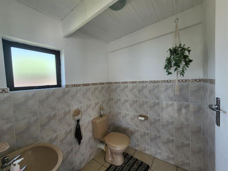 A functional bathroom featuring tiled walls and flooring, a basin, and a toilet, with a timber ceiling and frosted window for natural light.