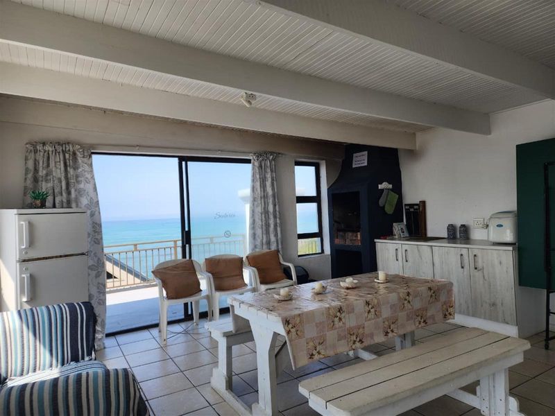 Open-plan living area featuring tiled floors, exposed beam ceilings, a built-in fireplace, and sliding doors leading to a balcony with ocean views.