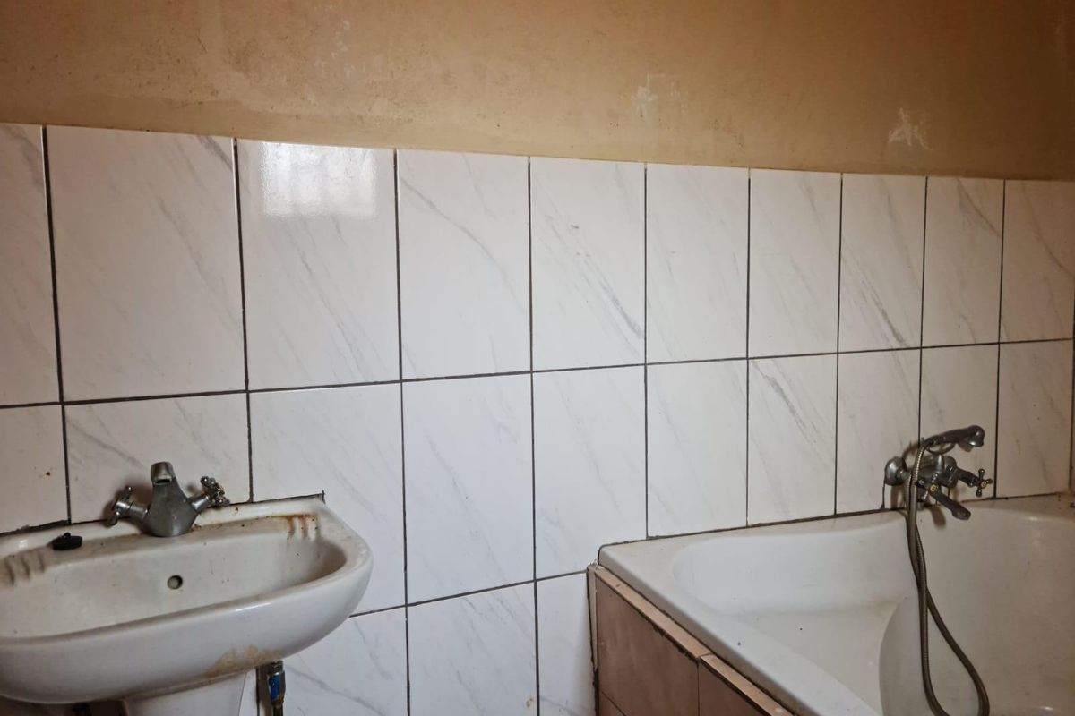 A bathroom featuring a pedestal basin and bathtub with tiled splashbacks, requiring cosmetic updates and maintenance to the fixtures and wall finishes.