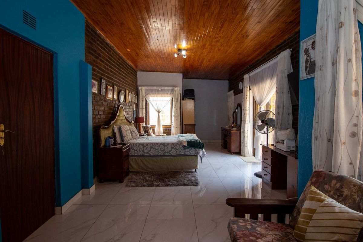 Spacious bedroom featuring polished tile flooring, a warm timber-clad ceiling, and a distinctive exposed brick feature wall.