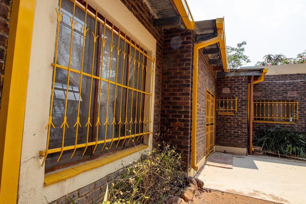 Exterior view of the house featuring face brick walls, yellow painted window frames, and security bars over the windows.