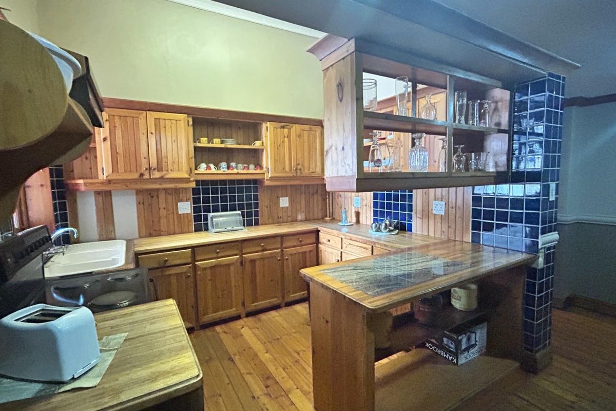 A traditional kitchen featuring timber cabinetry, a breakfast bar, and blue tiled splashbacks with wooden flooring.