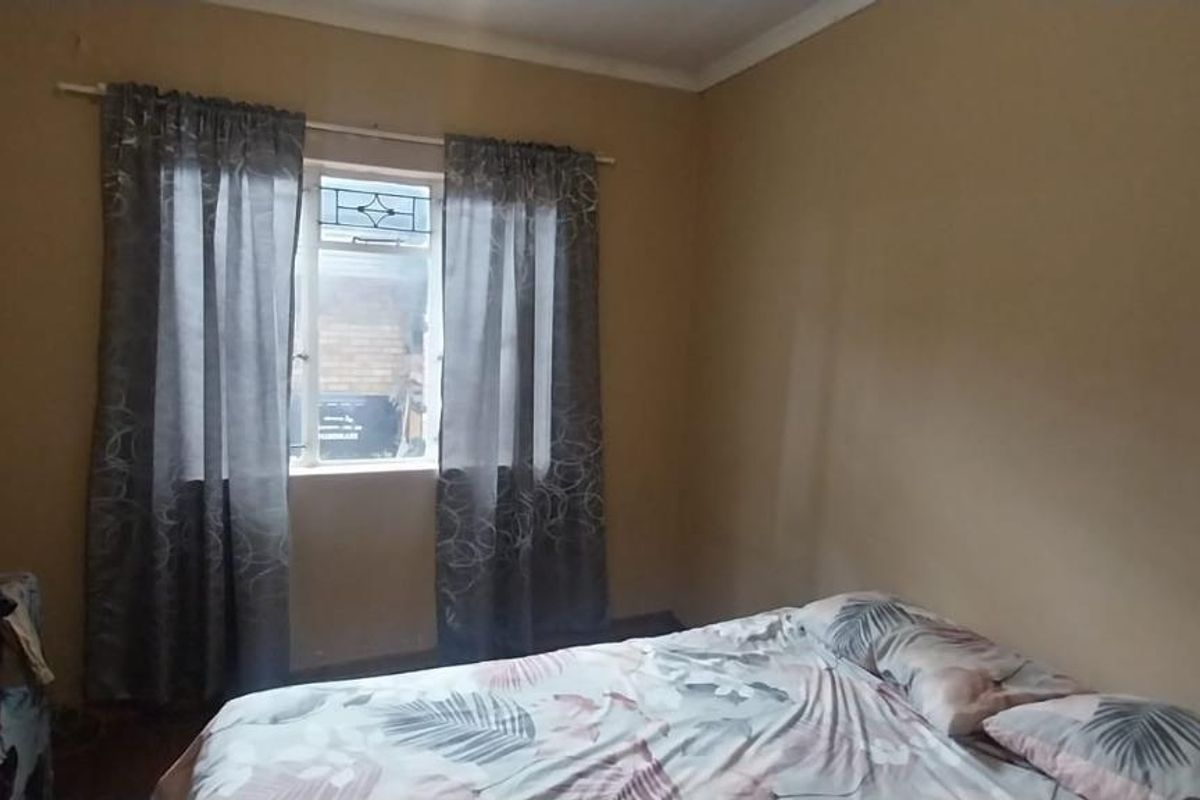 A simple bedroom featuring a single window with curtains and neutral wall finishes, offering a blank canvas for potential updates.