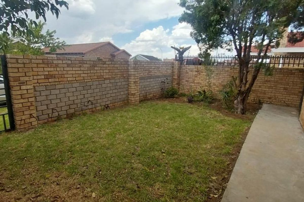 A private rear garden area featuring a lawn, concrete pathway, and perimeter brick boundary walls with metal security fencing.