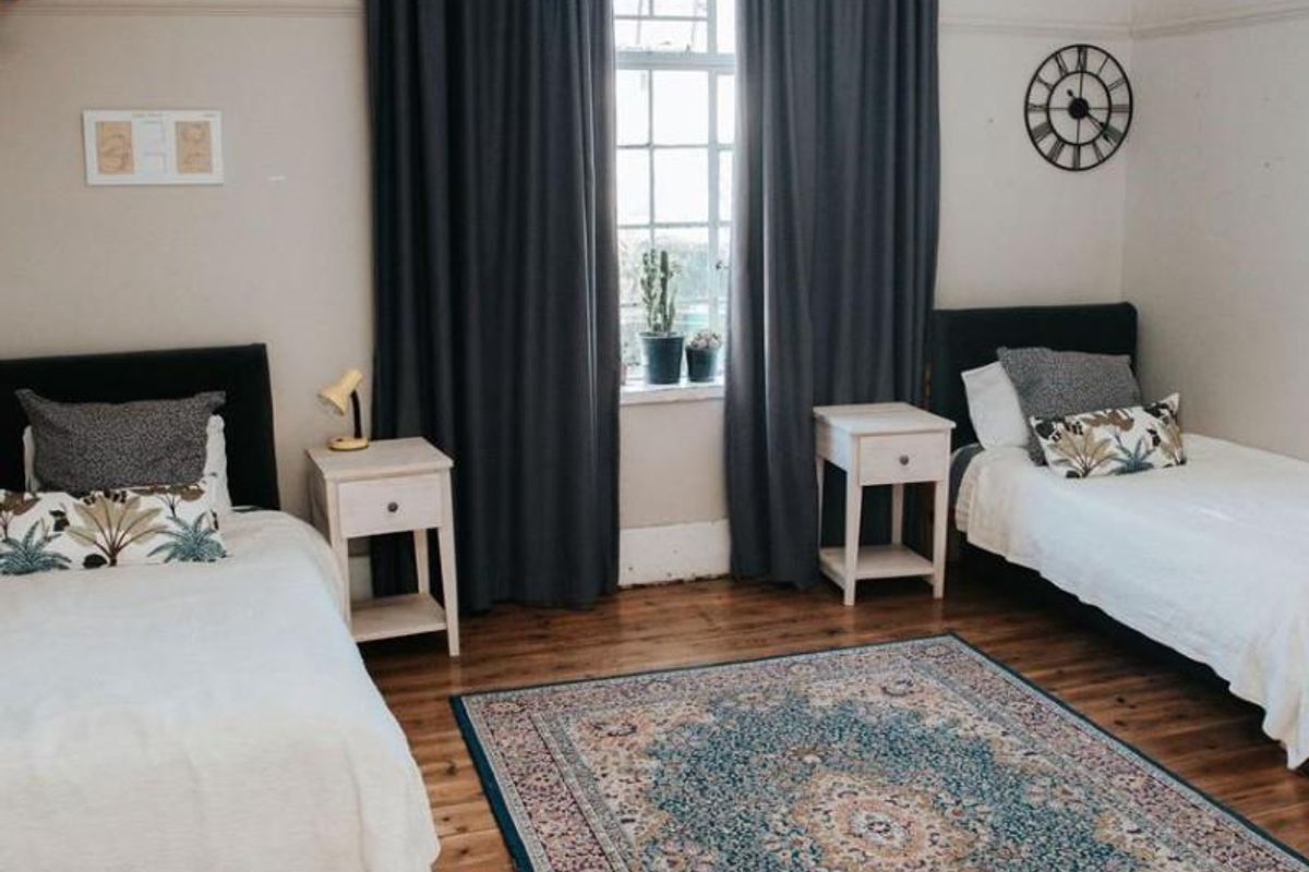 A spacious bedroom featuring polished timber flooring, high ceilings with picture rails, and a large window providing natural light.