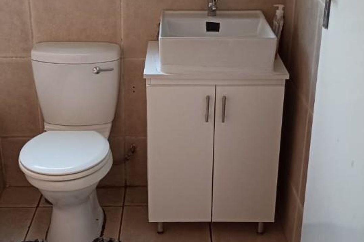 A compact bathroom featuring ceramic floor and wall tiling, a white vanity cabinet with a vessel sink, and a standard toilet.