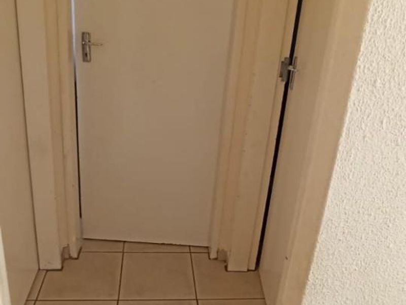A narrow hallway featuring tiled flooring and multiple internal doors, showing signs of wear on the frames and skirting.