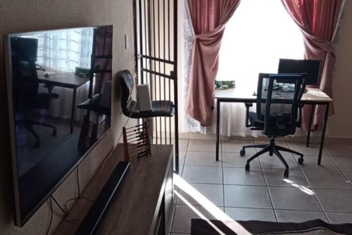 A living area featuring tiled flooring, a security gate, and large windows with curtains, providing natural light and access to the exterior.