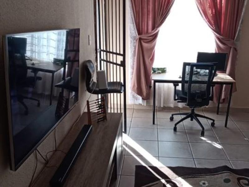 A living area featuring tiled flooring, a security gate, and large windows with curtains, providing natural light and access to the exterior.