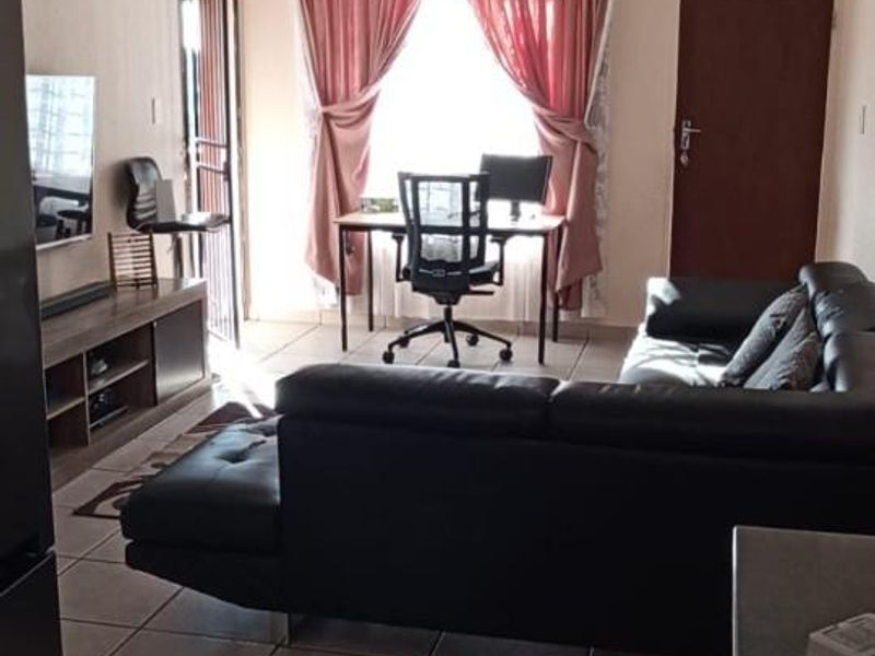 Open plan living area featuring tiled flooring, a security gate, and neutral wall finishes, providing a functional and connected space.