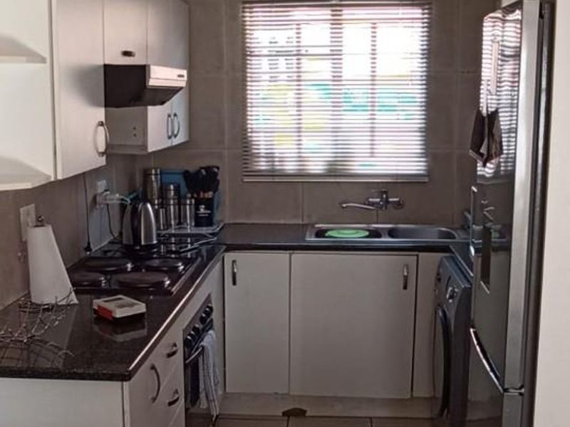 Compact kitchen featuring white cabinetry, granite countertops, built-in oven and hob, and tiled finishes throughout.