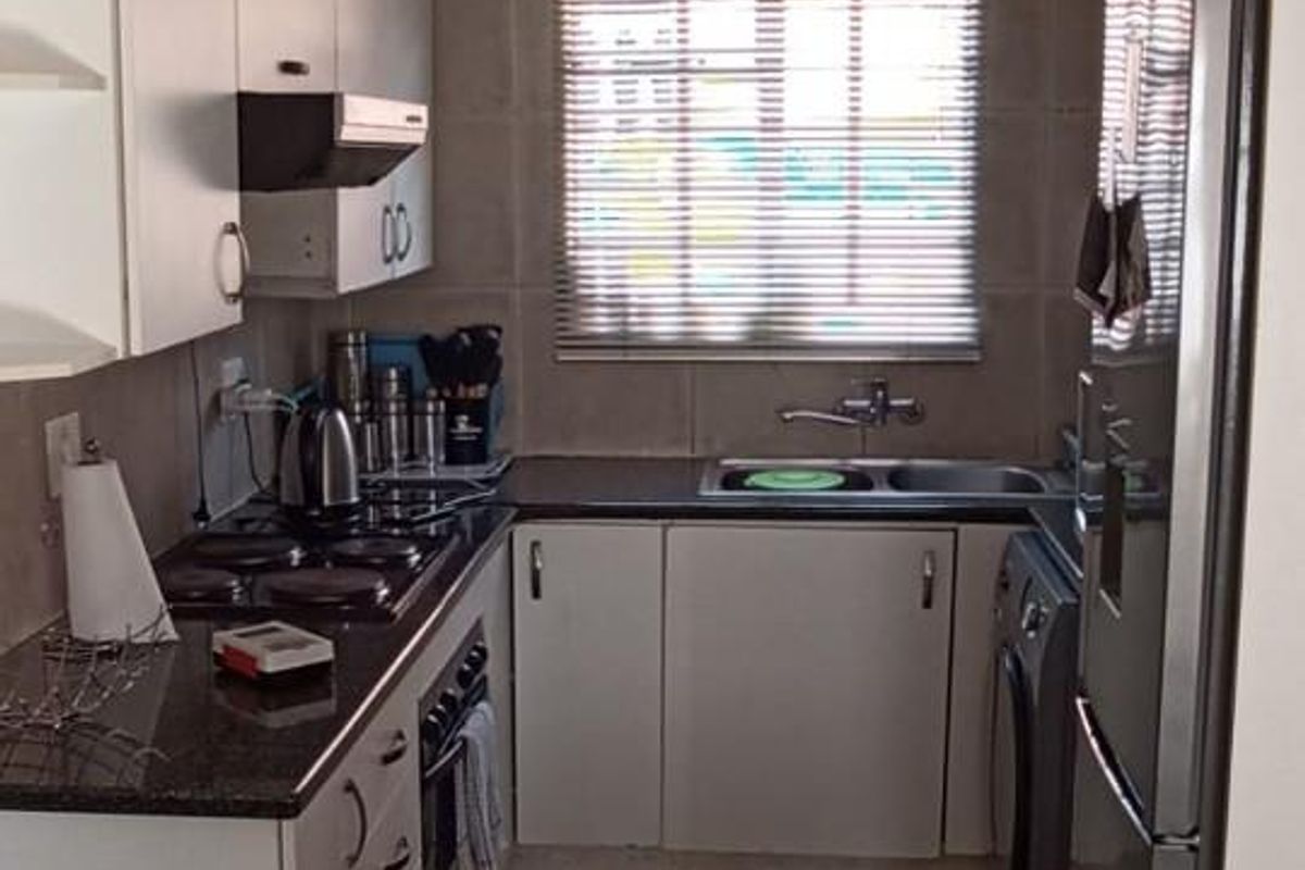 Compact kitchen featuring white cabinetry, granite countertops, built-in oven and hob, and tiled finishes throughout.