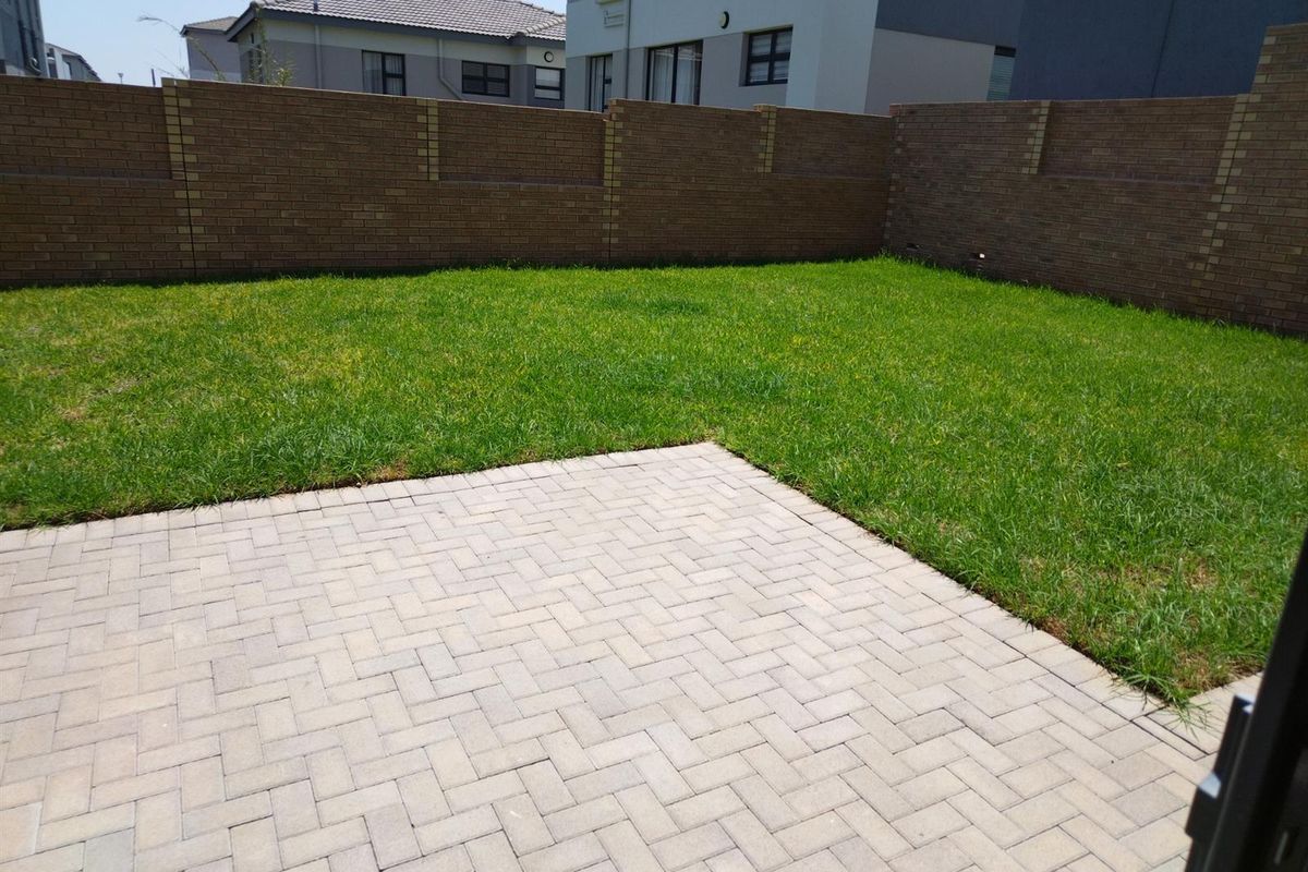 A private rear garden featuring a paved patio area and a well-maintained lawn, enclosed by perimeter brick boundary walls.