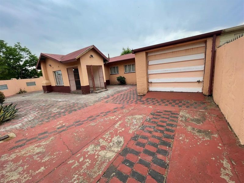 Front exterior view of the house featuring a paved driveway, attached garage, and covered entrance area with security gates.