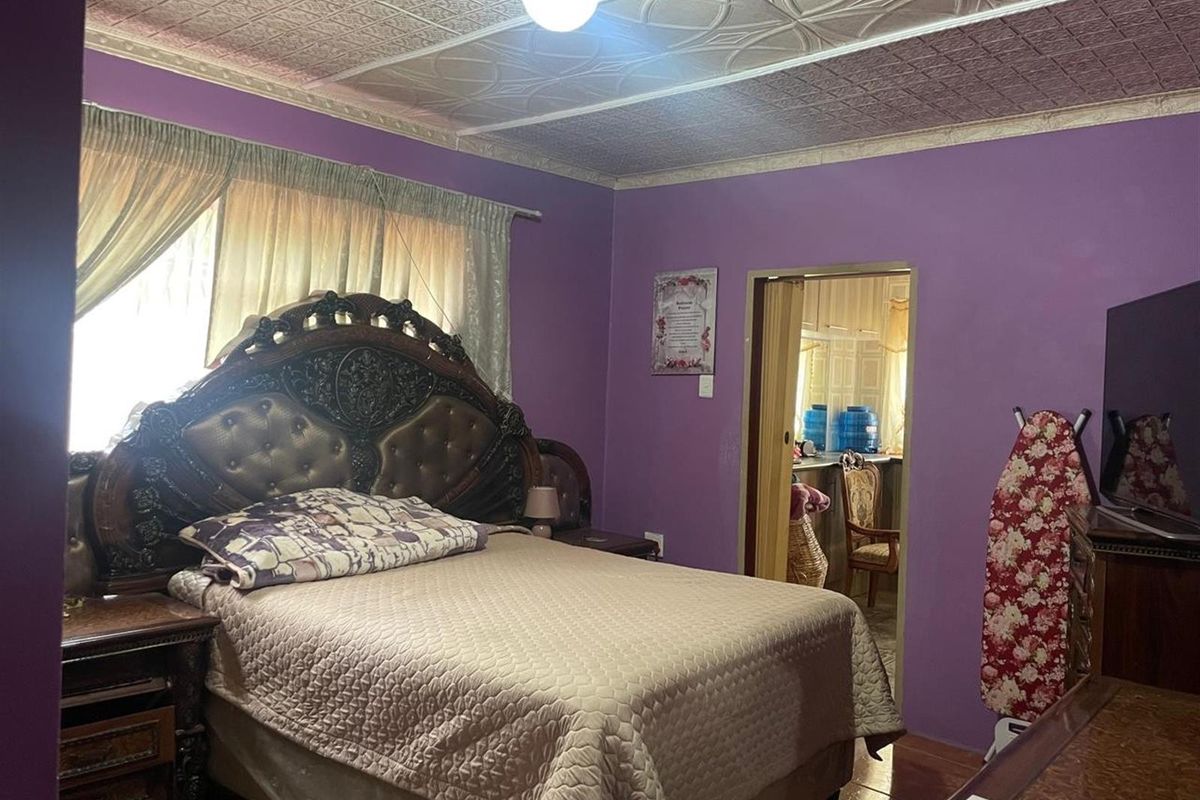 A bedroom featuring purple walls and decorative ceiling tiles, with an adjacent doorway leading to another room.