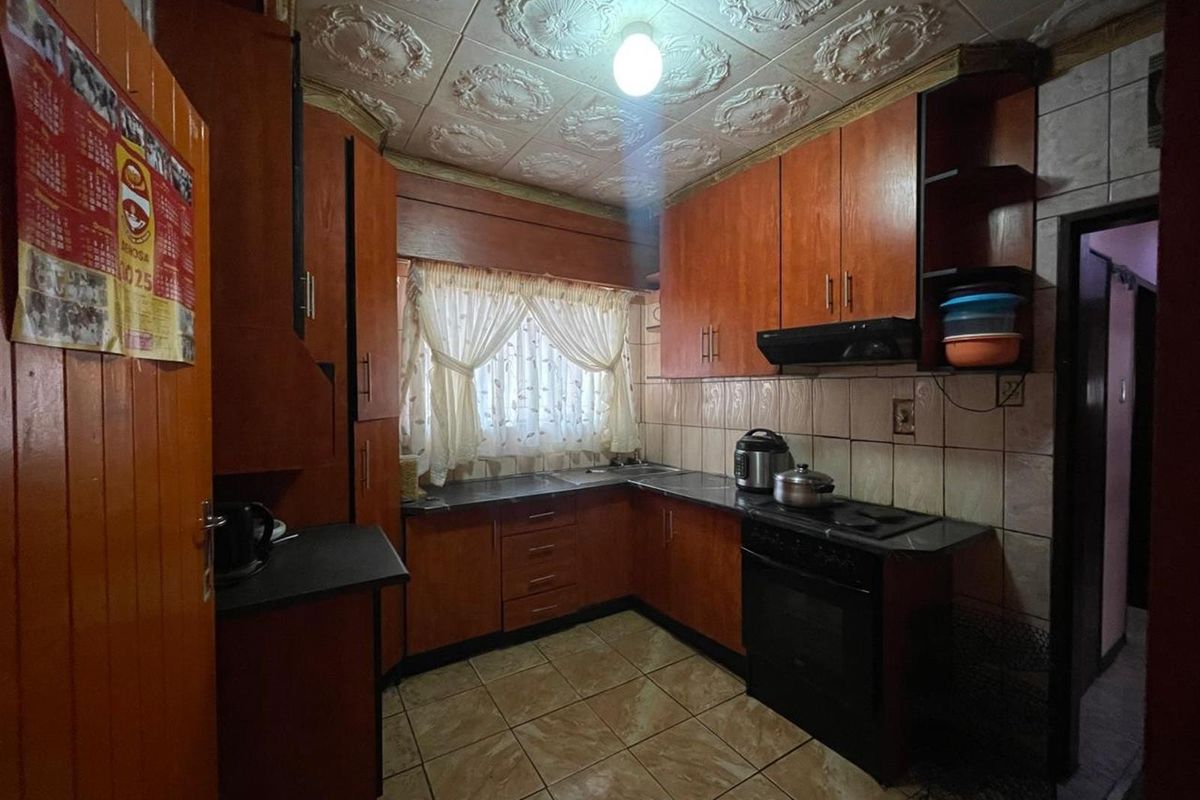 A compact kitchen featuring dark wood cabinetry, tiled countertops, and a decorative patterned ceiling, offering a functional layout in need of modernization.