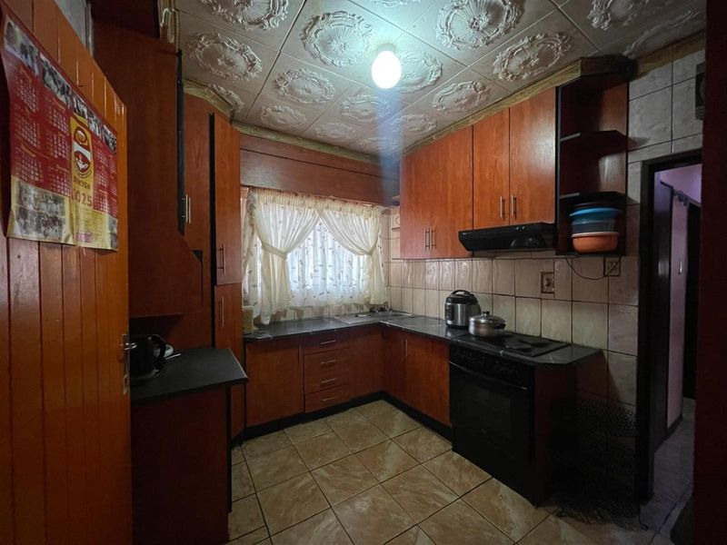 A compact kitchen featuring dark wood cabinetry, tiled countertops, and a decorative patterned ceiling, offering a functional layout in need of modernization.