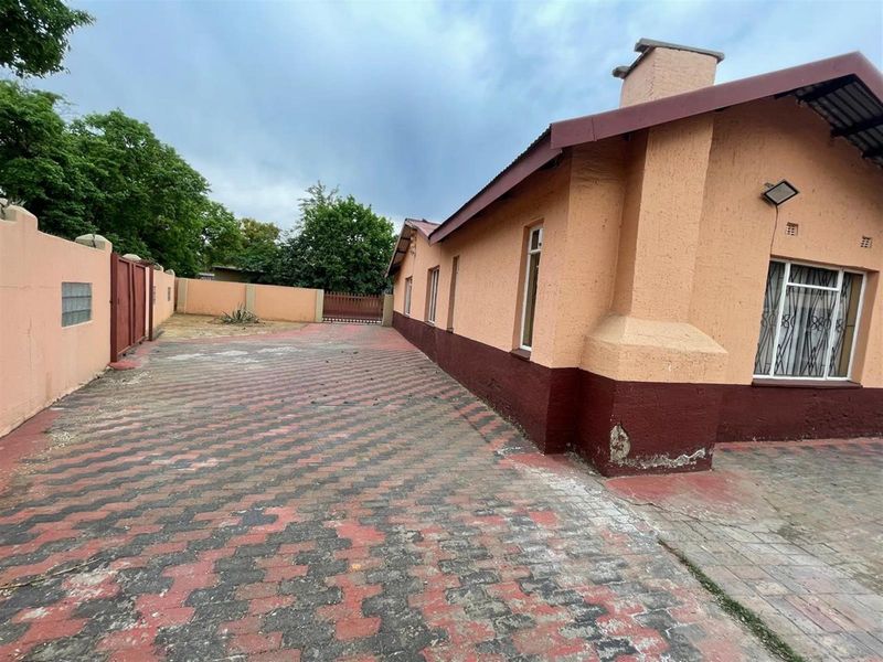 Side exterior view of the house featuring paved driveway, perimeter wall, and textured facade with visible signs of wear and maintenance requirements.