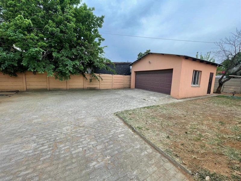A paved driveway leading to a detached garage with a sectional door, enclosed by a perimeter wall and featuring a small garden area.