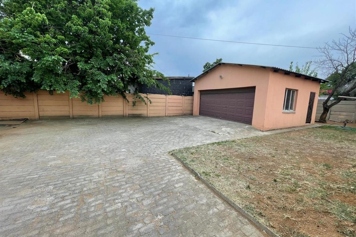 A paved driveway leading to a detached garage with a sectional door, enclosed by a perimeter wall and featuring a small garden area.