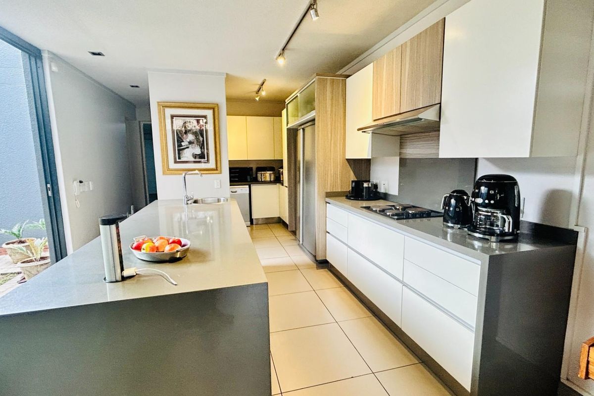 Modern kitchen featuring a large central island, stone countertops, integrated appliances, sleek cabinetry, and direct access to an outdoor patio area.