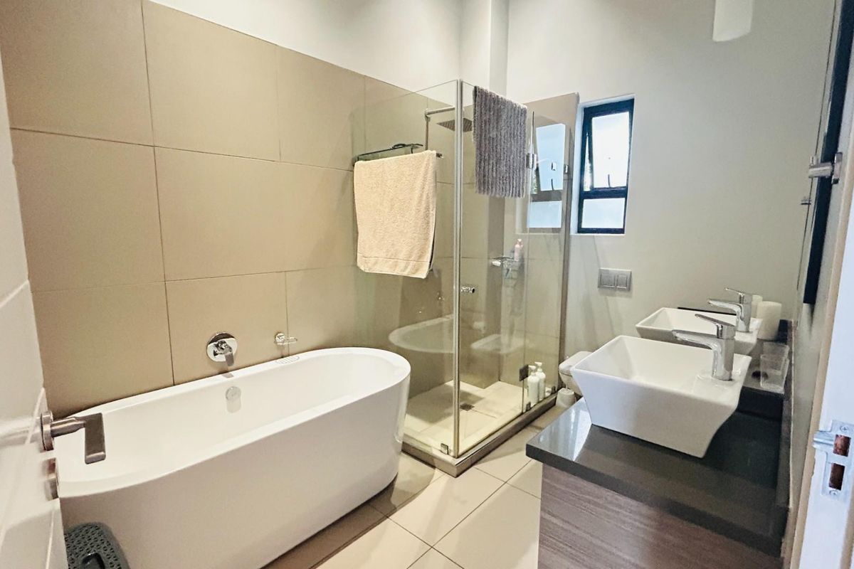 Modern bathroom featuring a freestanding bathtub, glass-enclosed shower, and a double vanity with vessel sinks and stone countertops.
