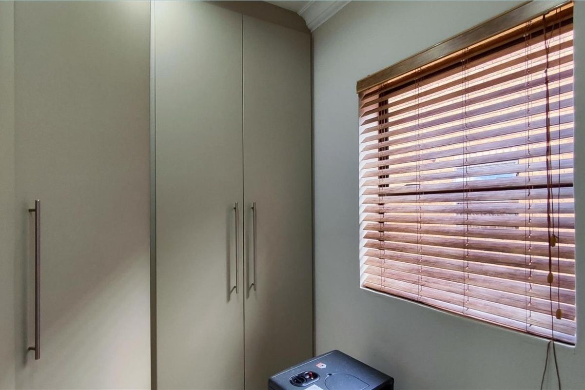 A bedroom featuring built-in cabinetry with modern handles and a window fitted with wooden venetian blinds.