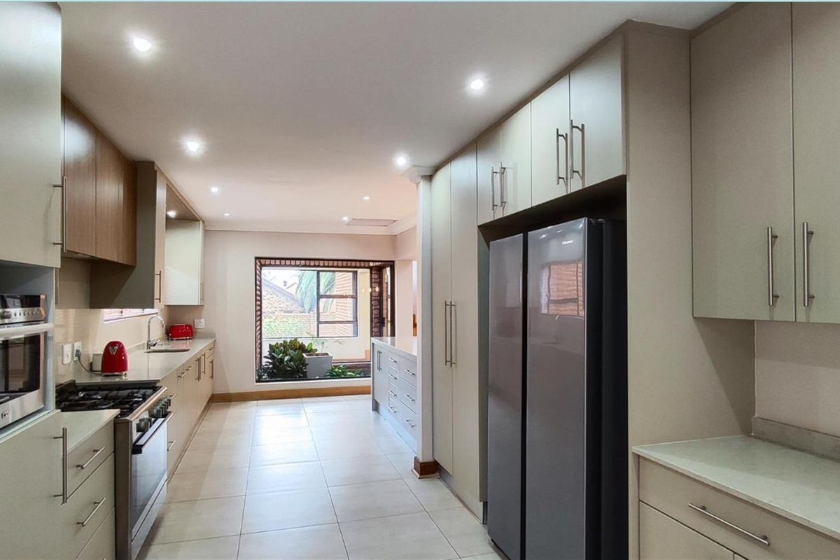 Modern kitchen featuring sleek cabinetry, integrated oven, gas cooktop, and tiled flooring, leading to a bright, open-plan space with a large window.