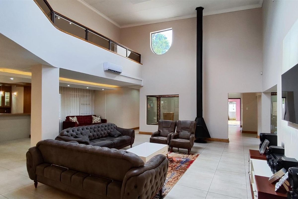 Spacious double-volume living area featuring a modern suspended fireplace, tiled flooring, and a mezzanine balcony overlooking the main lounge space.